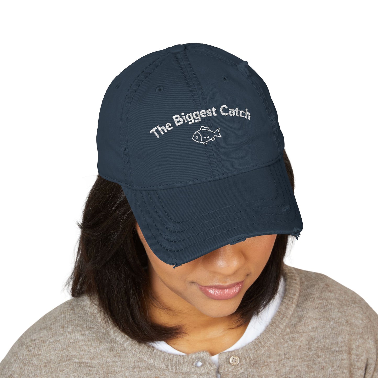Navy blue cap with 'The Biggest Catch' text worn by a person on a white background